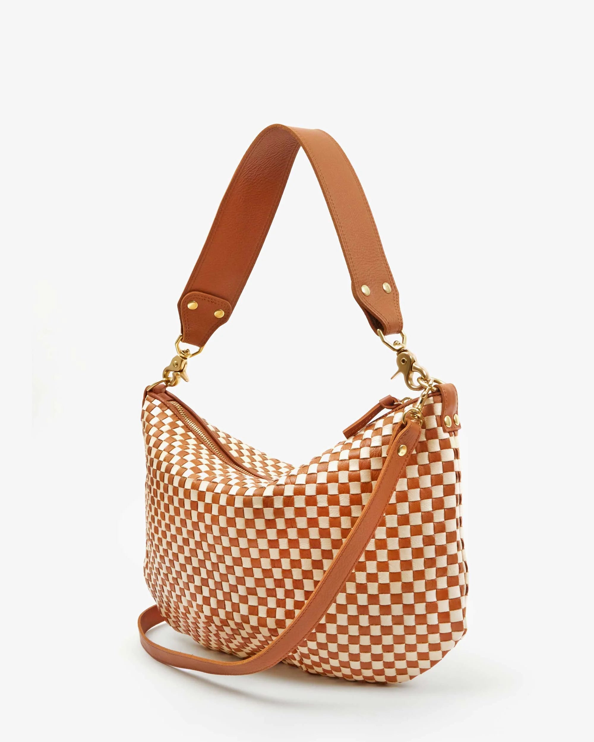 The Moyen Messenger by Clare Vivier is a slouchy, handwoven leather handbag with a brown and white checkerboard pattern. It features a brown leather crossbody strap, gold hardware, a detachable adjustable shoulder strap, and is set against a plain white background.