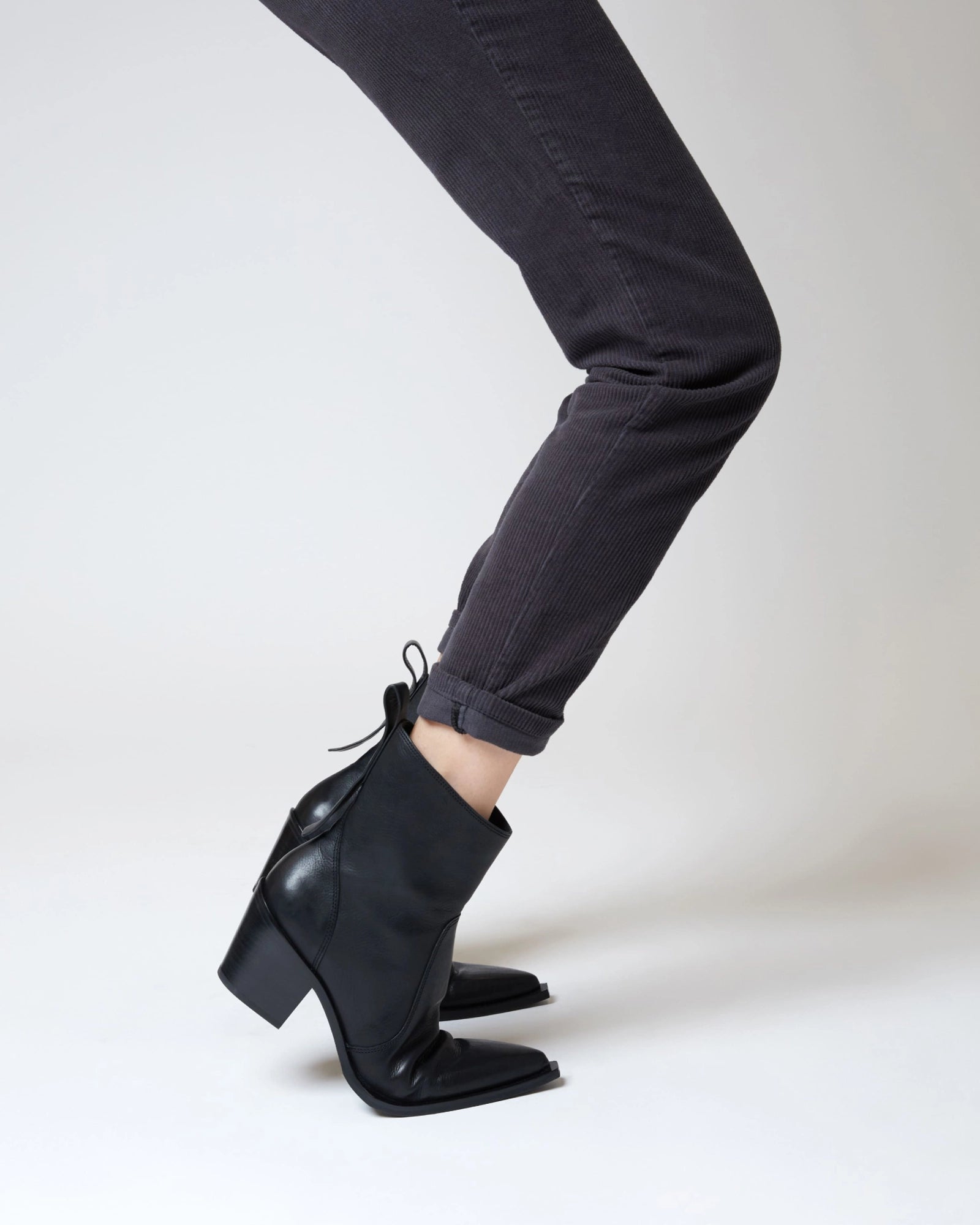 Wearing fitted dark gray pants and ONCEPT's Nashville Boot—genuine leather ankle boots with pointed toes and block heels—a person stands against a plain, light background.