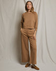 A woman stands against a light backdrop, wearing the Mikos Travel Wideleg Pant by Perfectwhitetee with a matching long-sleeve top. She finishes the look with brown loafers, one hand in her pocket and a relaxed expression.