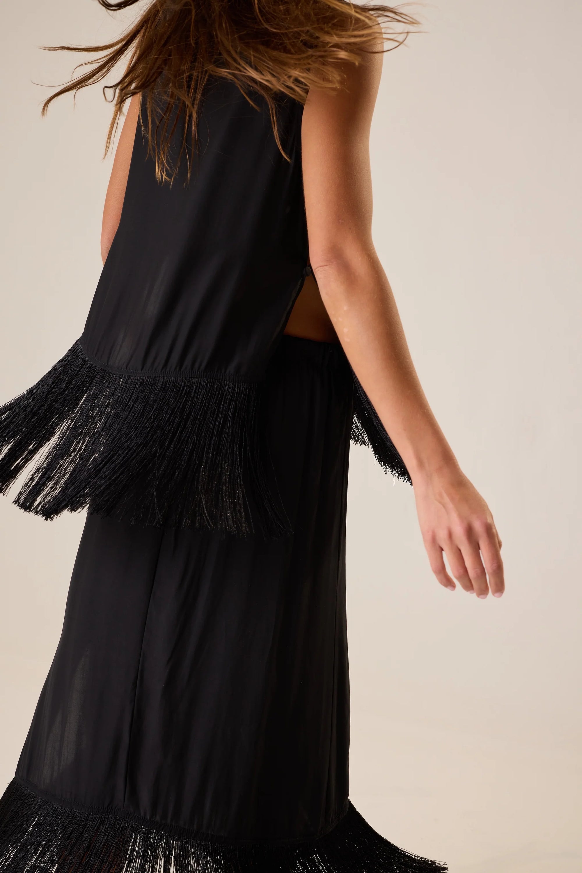 Natalie Martin Jessie Top in silk with fringe hem, sleeveless, modeled outdoors with windblown hair and outstretched arm.