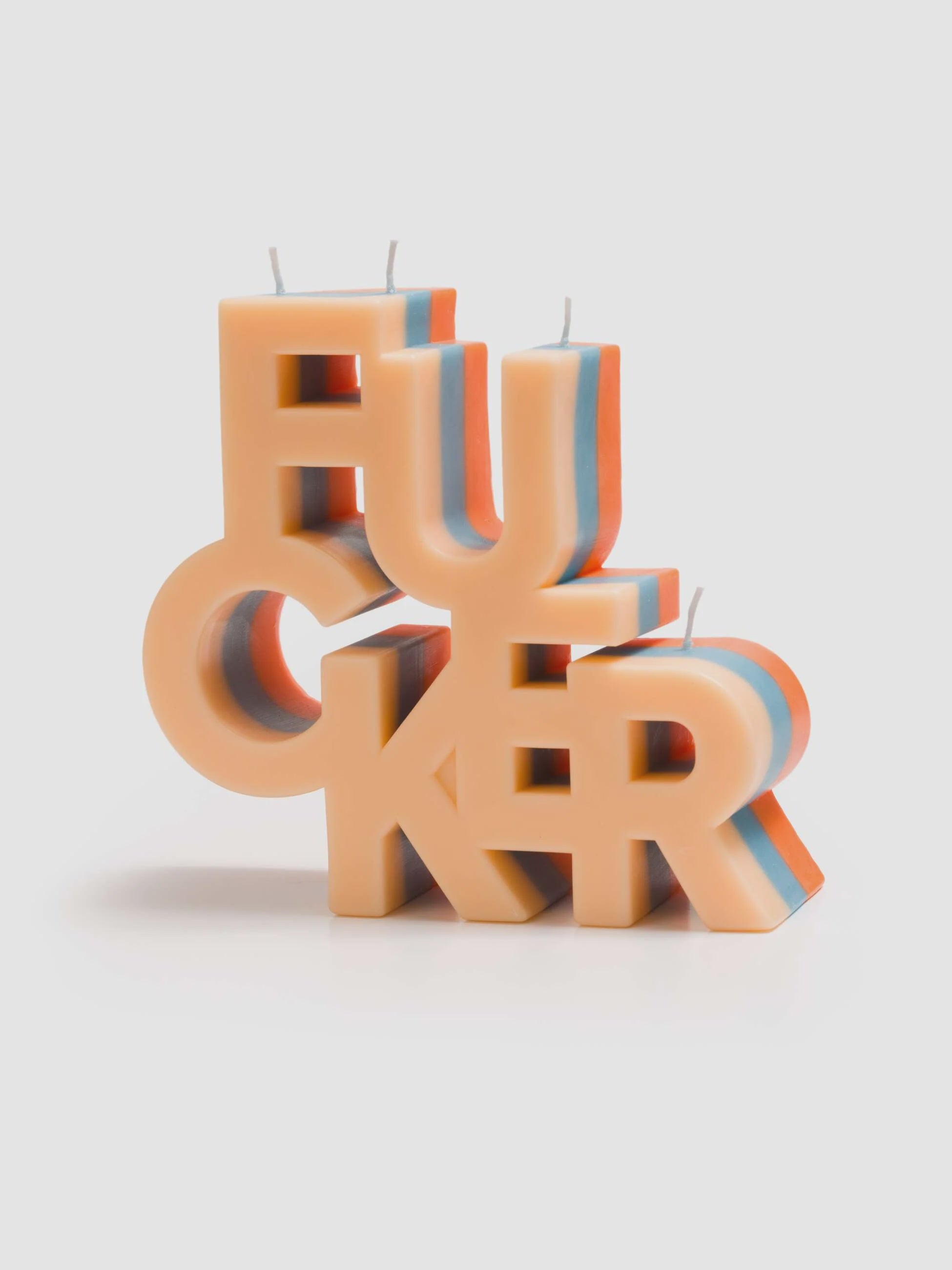 The Mother Burnout F..CKER Candle by Mother features block letters crafted from beige, red, and blue soy wax with five wicks, shown on a plain white background.