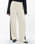 A person wears Rag & Bone's olivia stripe pant—relaxed fit, wide-leg cream pants with black side panels—paired with a black long-sleeve flared top and black shoes, standing against a plain white background.