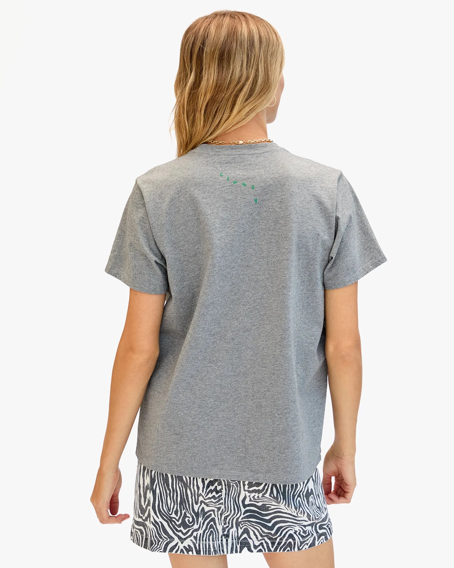 A person with long, light brown hair is shown from the back, wearing a Clare Vivier Original Tee Snake gray 100% cotton t-shirt and black-and-white patterned shorts, standing against a plain white background.