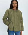 A person with long dark hair is wearing a Pistola Elva Onion Stitch Puffer Jacket in olive green, featuring onion stitch quilting, front buttons, and pockets. They have a neutral expression and are standing against a plain, light-colored background. Additionally, they are wearing blue jeans.