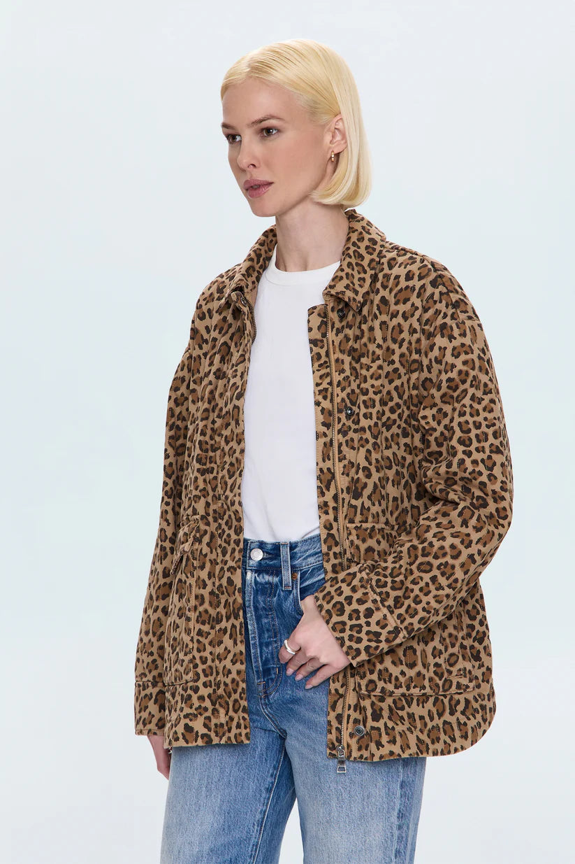 A woman with short blonde hair models the Pistola Cecile Quilted Jacket in leopard print over a white t-shirt and blue jeans, standing against a plain light background.
