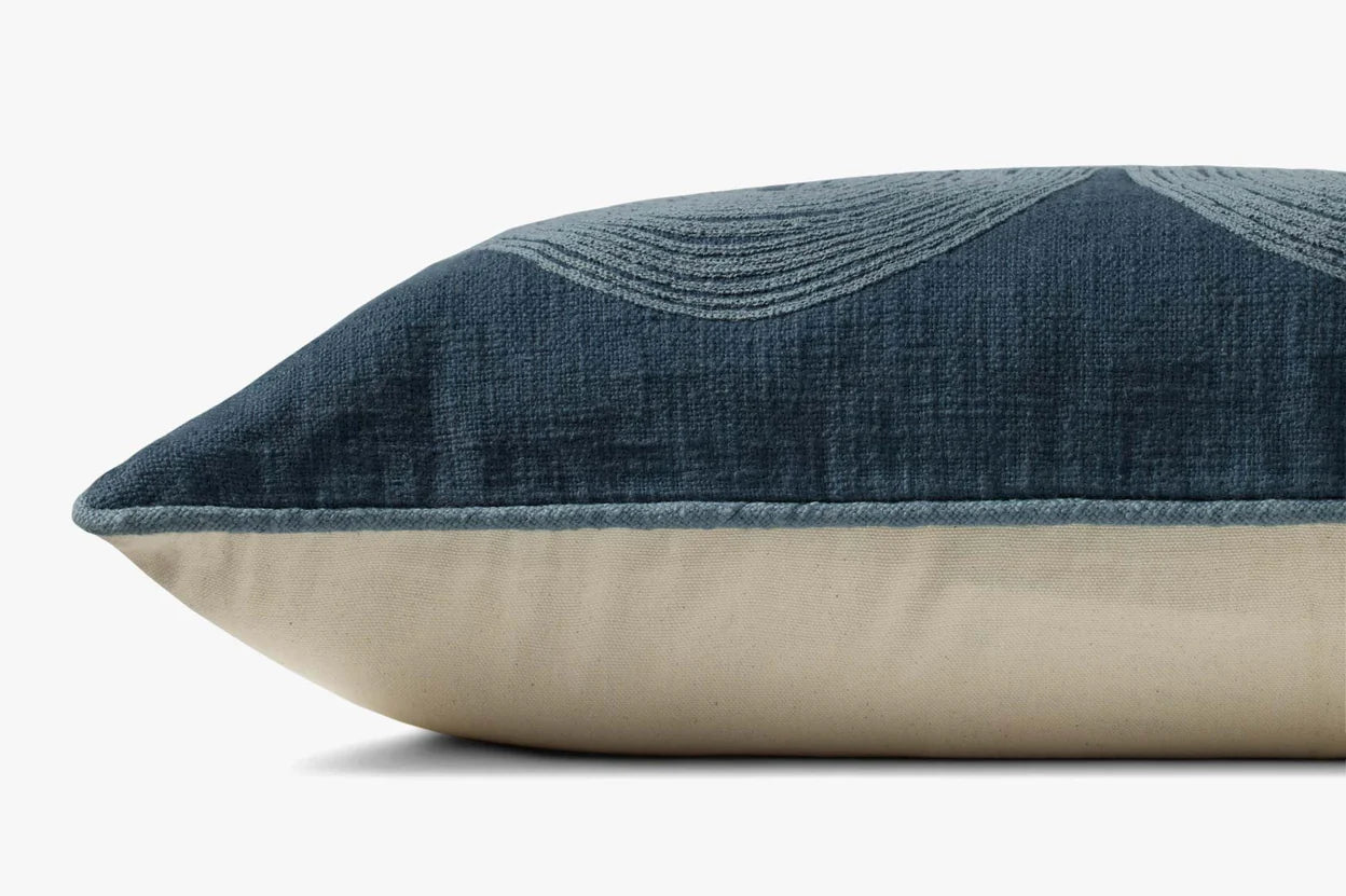 A close-up side view of the Loloi Rugs PBR0004 Navy Pillow shows its rectangular shape, blue textured cotton top with a curved embroidered pattern, beige bottom, and discreet zipper along one edge.