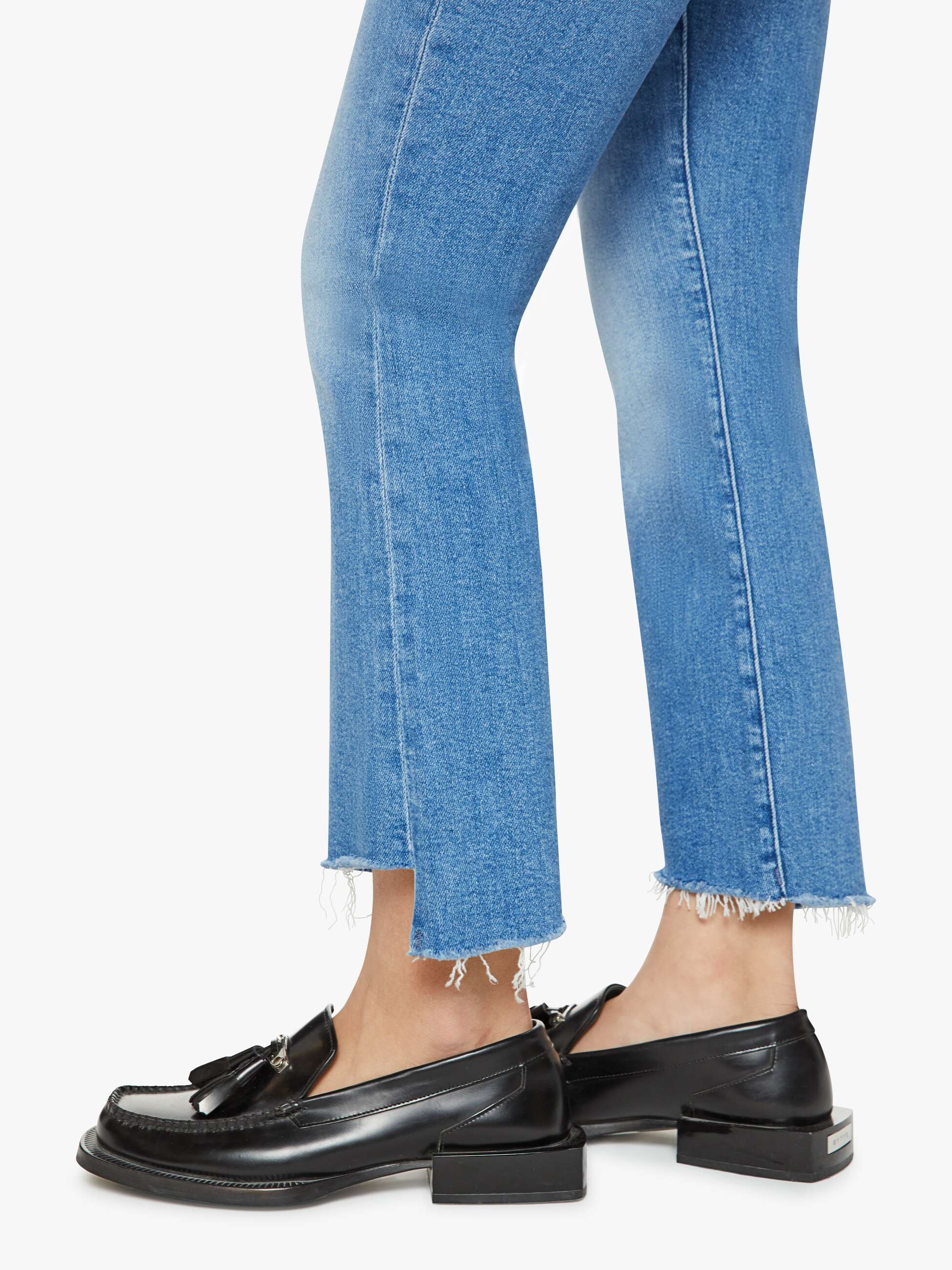 Cropped view of a person wearing Mother’s Lil Insider Crop Step Fray jeans and black leather loafers with tassel details, standing against a white background.