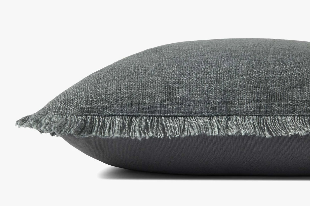 Close-up of the Loloi Rugs Sable Blue 22x22 pillow: a rectangular, dark gray machine-woven cushion in textured polyester-cotton-linen blend with fringe trim and hidden flap zipper, shown against a plain white background.