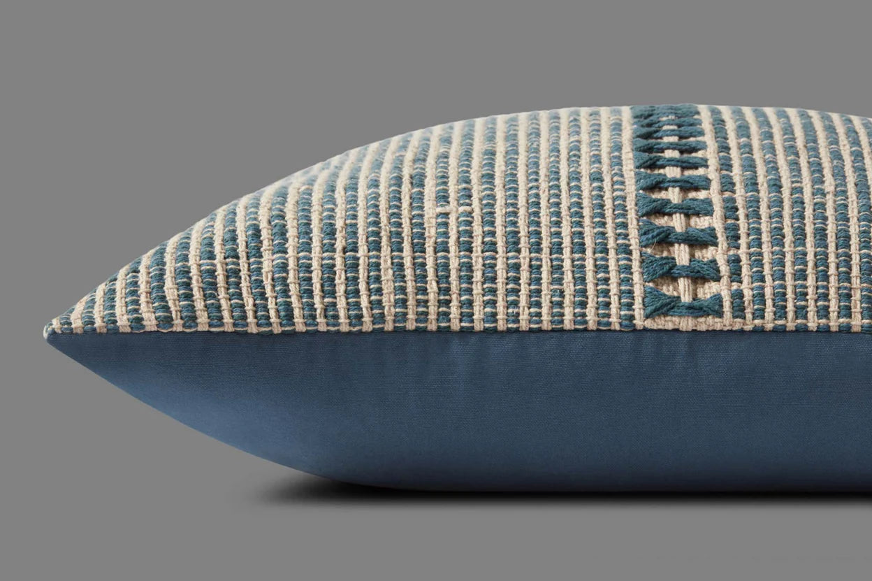 The Loloi Rugs PCJ0018 Blue Natural pillow combines cotton and polyester in a textured cream and blue woven design with stitched X patterns on top and solid blue fabric underneath, displayed against a plain gray background.