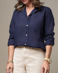 A person with wavy hair is wearing a navy blue Frank & Eileen BARRY Button Up Shirt with long sleeves rolled up to the elbows. They have paired it with light-colored pants, embodying a casual Arizona bungalow style. Multiple bracelets adorn one wrist and a watch on the other. The person's face is not visible.