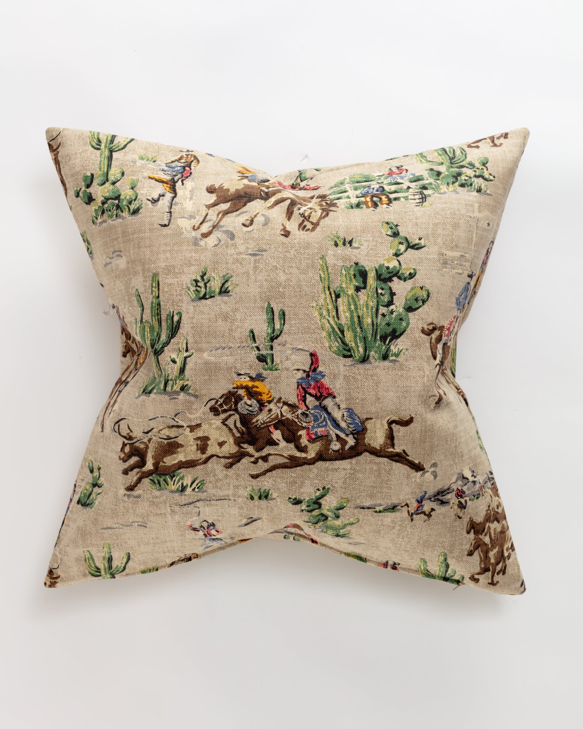 The Pindler Custom 2 Pillow 28x28 features a vintage-style cowboy print on a luxurious square pillow. Cowboys ride horses among cacti in a desert setting, with a neutral beige background accented by green, brown, and red tones. Includes pillow insert for added convenience.