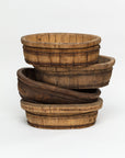 A stack of four rustic, round wooden baskets of varying sizes exudes rustic elegance. The handmade vintage baskets are slightly worn, displaying visible wood grain and metal bands that highlight their aged charm. They nest inside one another, creating a tiered arrangement against a plain white background. These are the Indus Design Imports Oval Wood Bucket 10.
