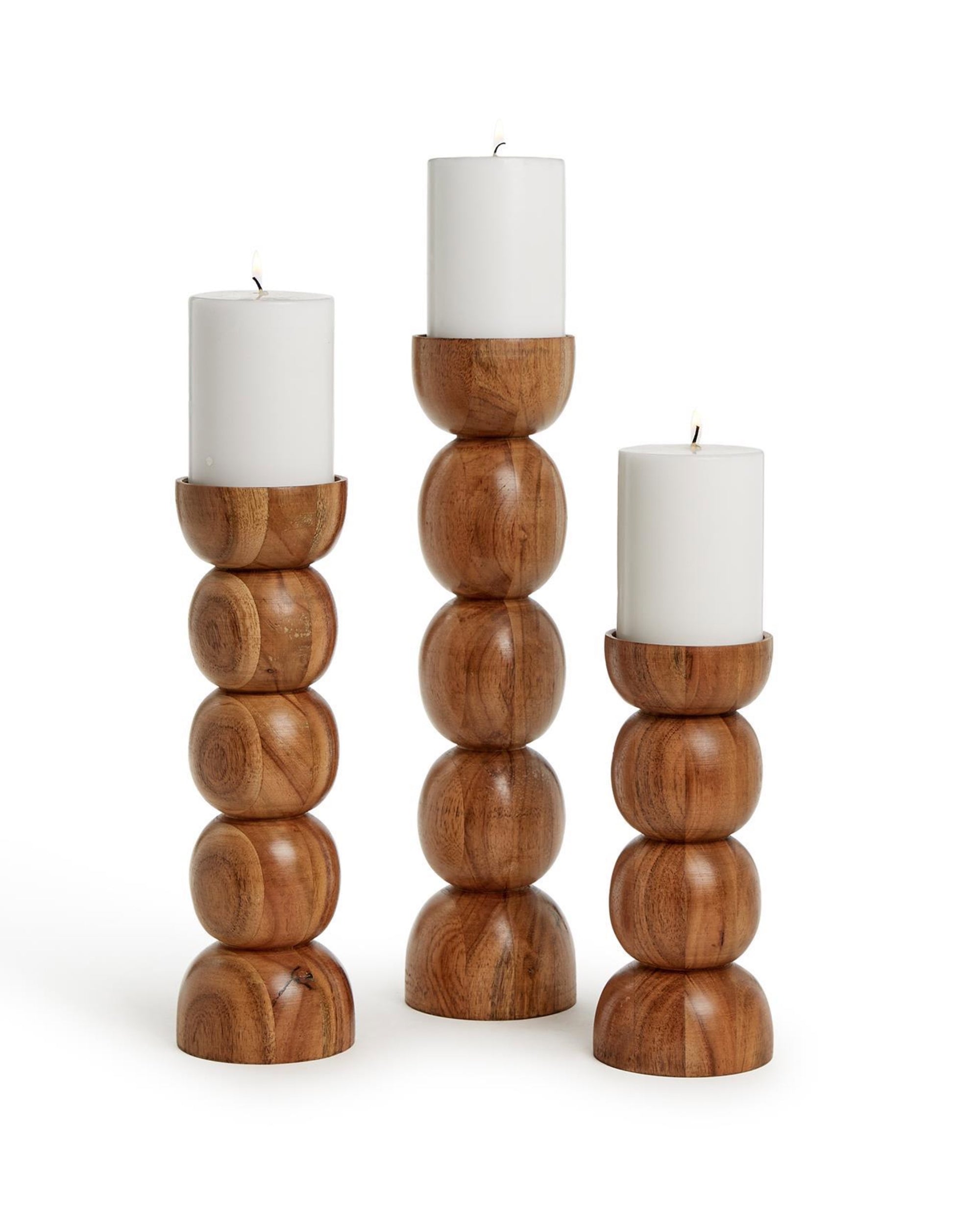The PDT001 Pillar Candleholders by Two's Company feature hand-crafted, stacked rounded shapes in natural wood finish, each holding a white pillar candle. Three varying heights are arranged side by side on a plain background.