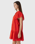 A woman with long brown hair wears the Pippa SS Mini Dress by Sea New York, a vintage-inspired red mini dress with lace accents, standing in profile against a plain light gray background.