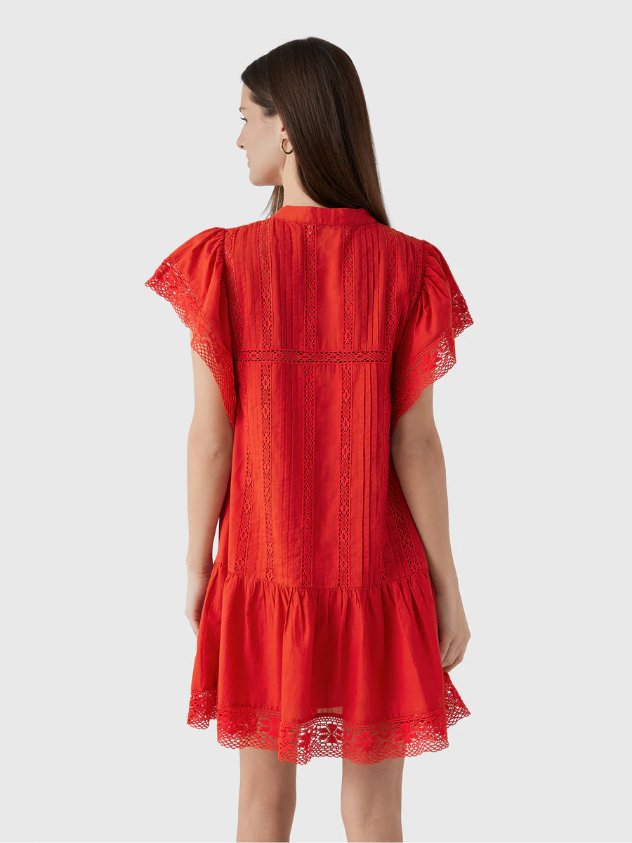 A woman with long brown hair is seen from the back wearing the Sea New York Pippa SS Mini Dress—a bright red, loose-fit mini with lace accents on the sleeves, hem, vertical seams, and ruffled trim at the bottom.