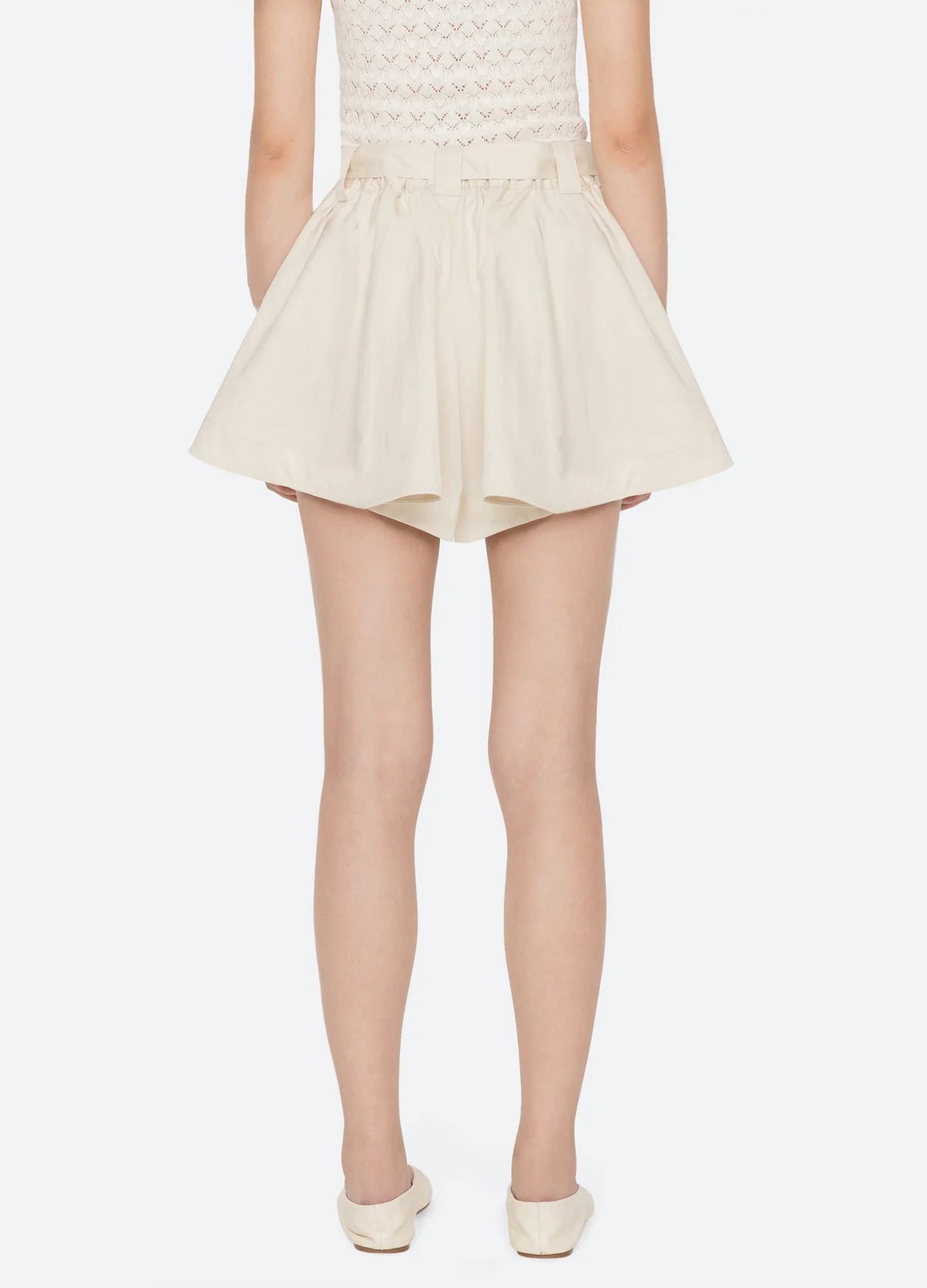 A person is shown from the back wearing Sea New York's Angelina Suiting Flare Shorts in cream with an elastic waistband, a sleeveless knit top, and cream flat shoes against a plain white background.