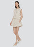 A woman with straight long hair stands against a plain background wearing the Sea New York Angelina Suiting Flare Short, a sleeveless beige button-up top, and matching beige flats. The shorts feature pleats and an elasticized waistband.