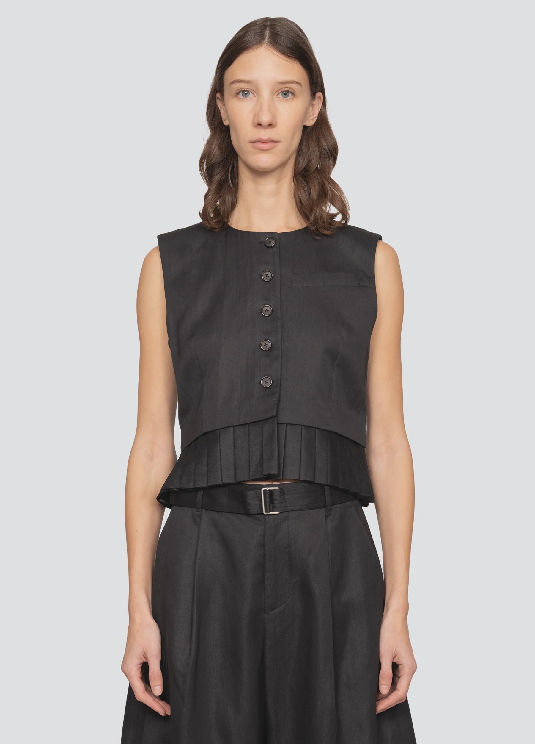 A woman with wavy brown hair wears the Sea New York Angelina Suiting Vest and belted high-waisted black trousers, standing facing forward against a plain light background.