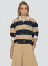 A woman wears the Sea New York Juliet SS Rugby with puff sleeves over a white collared shirt, paired with beige wide-leg pants and a dark braided belt, standing facing forward with one hand in her pocket.