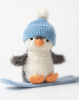 The Jelly Cat Inc. Peanut Penguin Snowboarding plush toy wears a light blue knit hat and stands on a small blue snowboard against a plain white background.