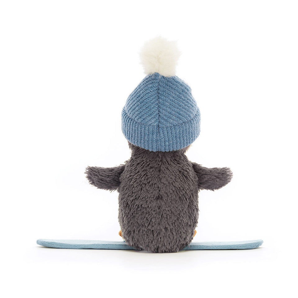 Peanut Penguin Snowboarding by Jelly Cat Inc. is a grey plush penguin wearing a blue knit hat with a white pompom, sitting on a blue snowboard, viewed from behind against a plain white background.