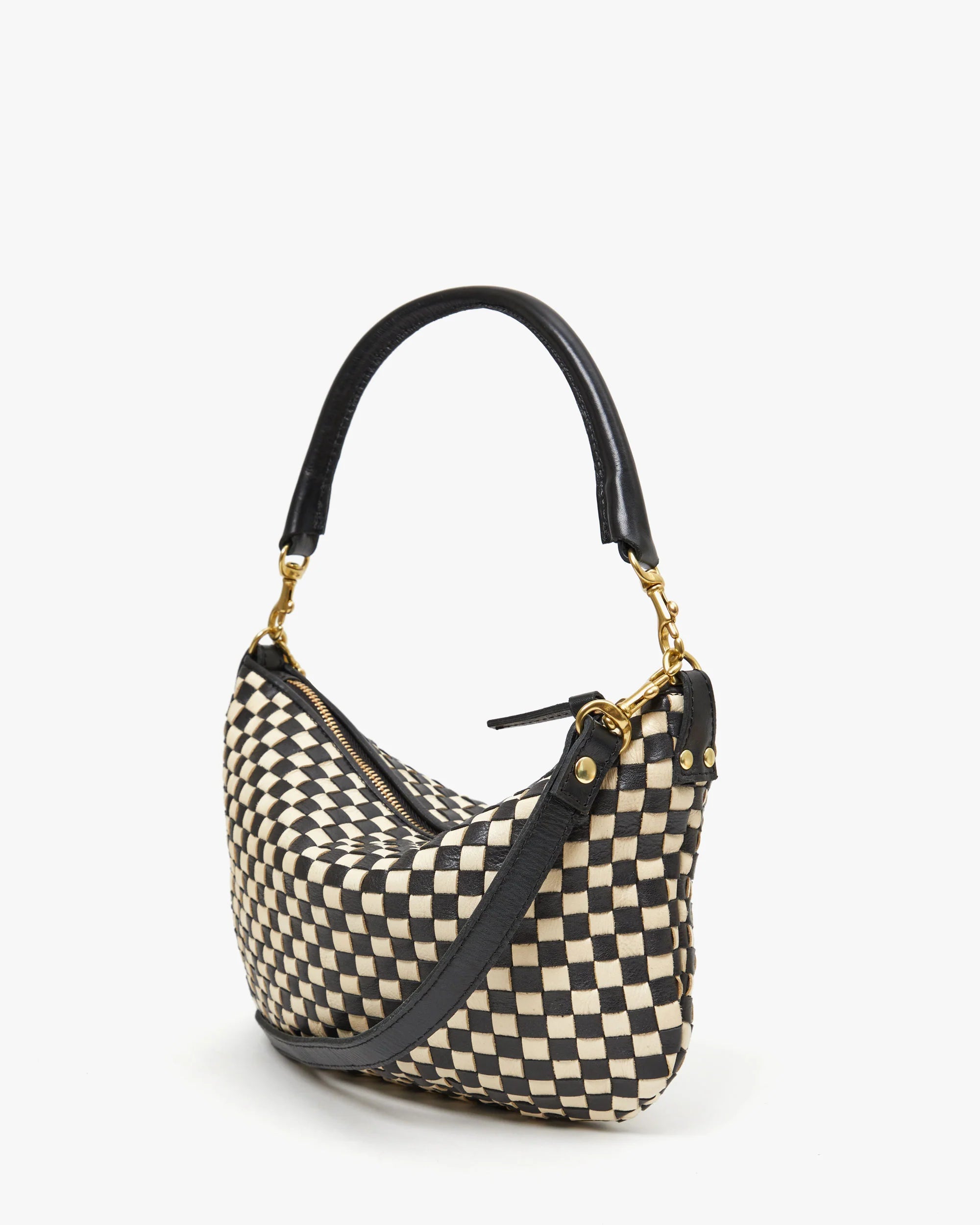 The Petit Moyen Woven Checker by Clare Vivier, a mini messenger handbag with a black and white checkered pattern and a black leather strap, is placed against a plain white background. The bag features gold hardware, including a zip closure and small studs on the strap connections.