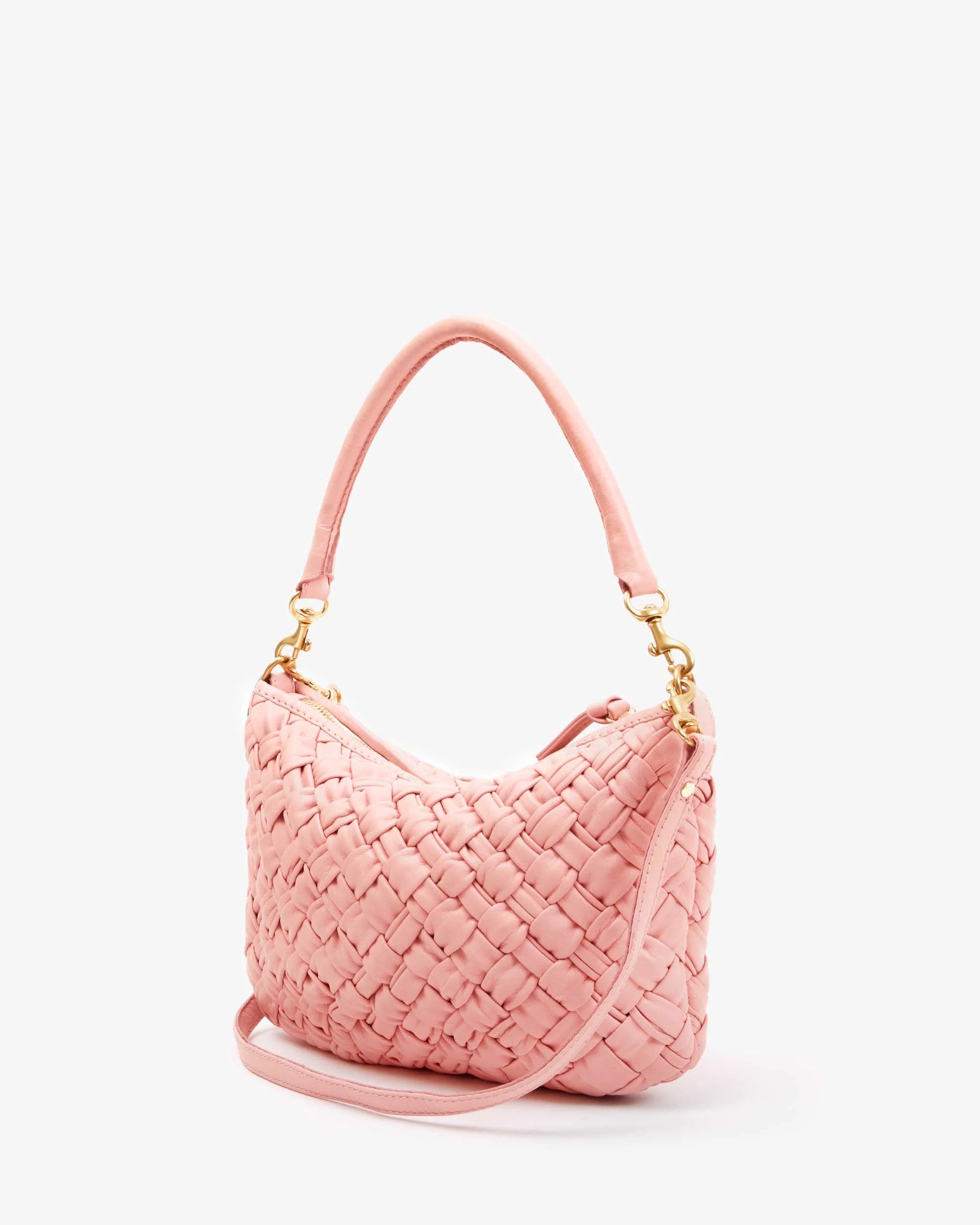 The Clare Vivier "Petite Moyen" is a pink handwoven leather handbag with gold-tone hardware, including hooks and a zipper. It has a short handle, detachable crossbody straps, and its woven texture gives it a stylish elegance against the white background.