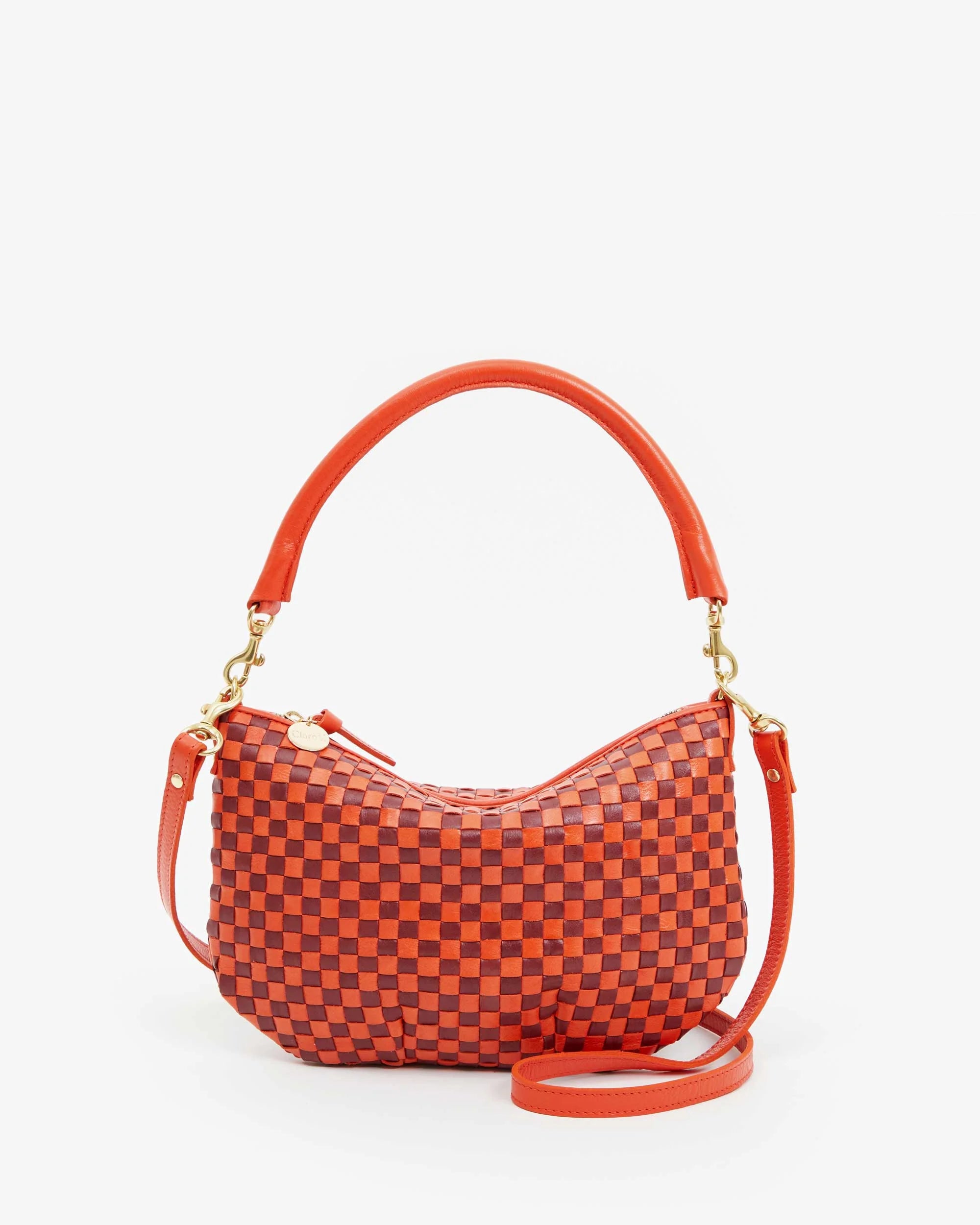 The Clare Vivier Petit Moyen Woven Checker is a handwoven leather handbag with an orange and red checkerboard pattern, featuring a curved handle, detachable orange shoulder strap, gold hardware accents, and a top zip closure.