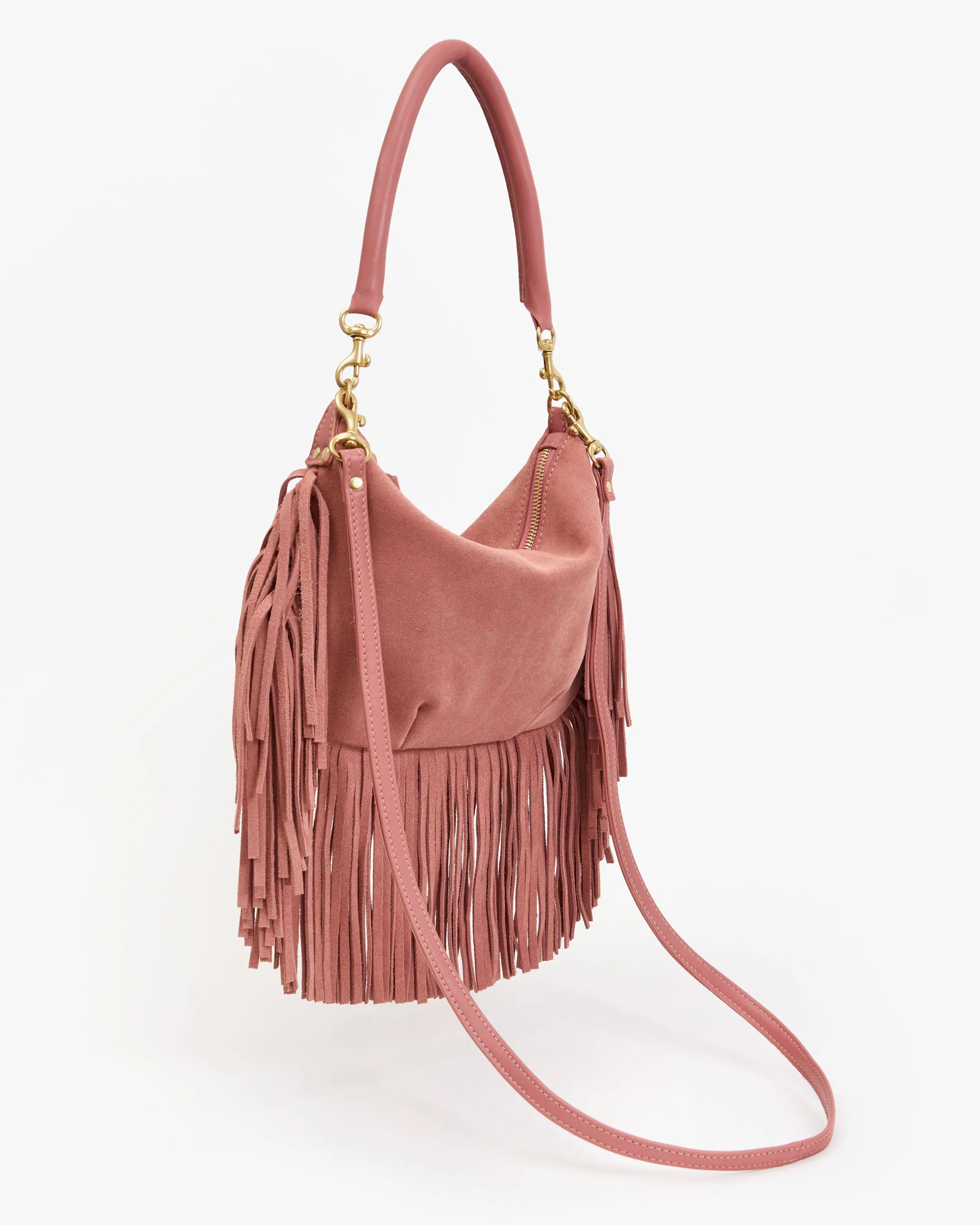 The Clare Vivier Petit Moyen Messenger Suede Fringe is a pink suede mini bag with gold hardware, top handle, crossbody strap, and fringe on the sides and bottom, displayed against a white background.