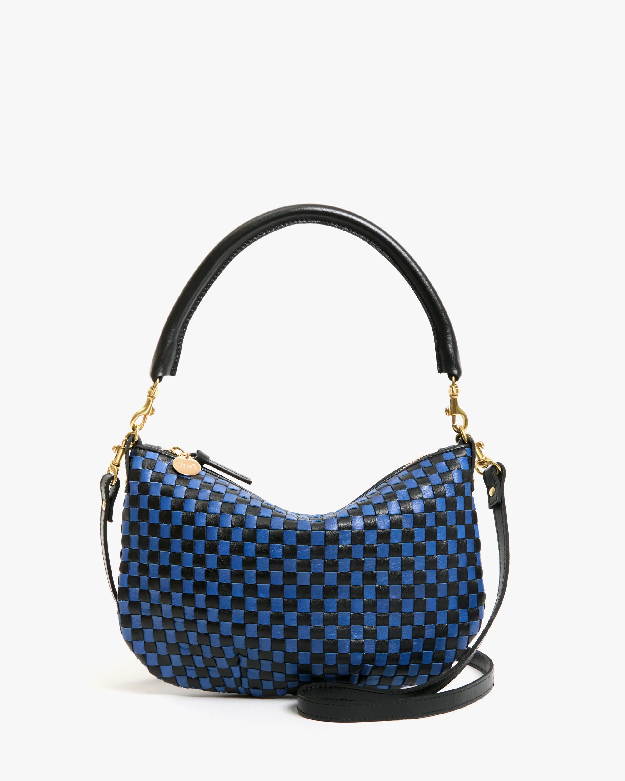 The Clare Vivier Petit Moyen Messenger S25 is a small, crescent-shaped mini messenger bag with a handwoven blue-and-black checkerboard leather pattern, gold hardware, a short black handle, and detachable crossbody straps.