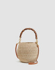 The Clare Vivier Petite Pot de Miel is a round, handwoven straw basket bag featuring a curved bamboo handle and a detachable brown leather shoulder strap, shown against a plain light background.