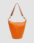 The Clare Vivier Petite Jeanne is a bright orange Italian leather bucket bag with a brown adjustable shoulder strap, gold hardware, and a small front pocket, shown against a plain white background.