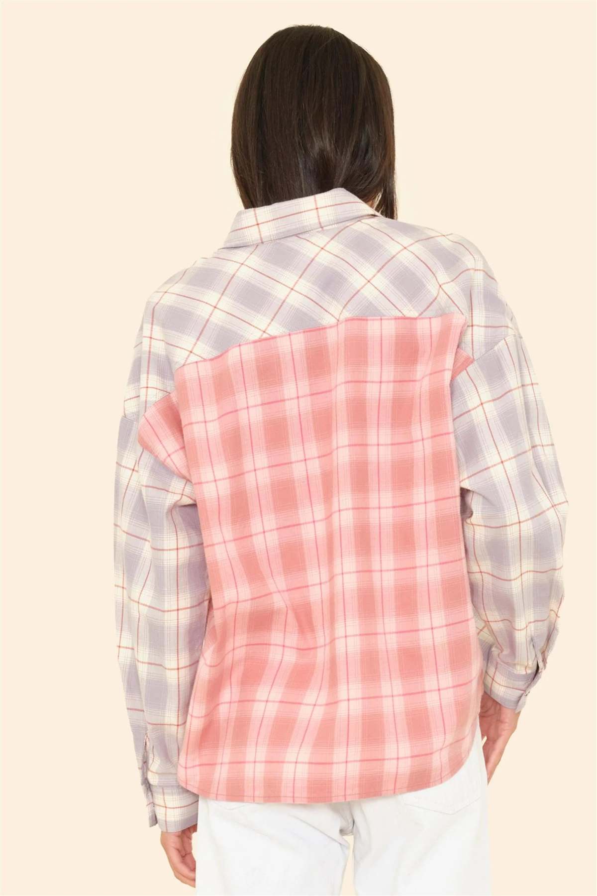 Shown from the back, the person wears the Xirena Phillipa Shirt—crafted from 100% cotton with light purple and pink plaid mismatched panels—paired with white pants for a relaxed style.