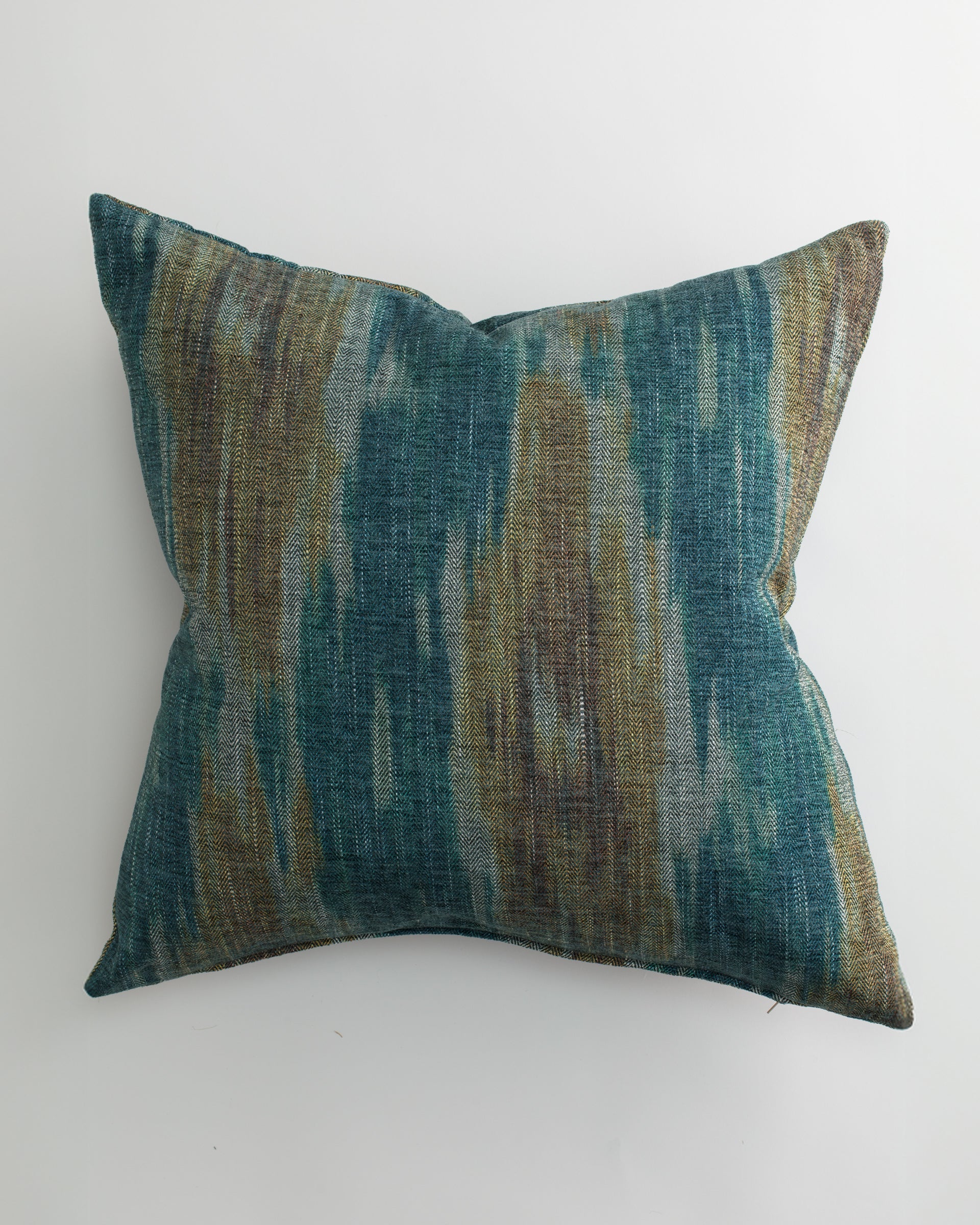 The RANDERS 26x26 Pillow by Pindler features a textured fabric cover with an abstract teal, blue, brown, and gray pattern. Shown on a white background, it includes a plush down feather insert for comfort.