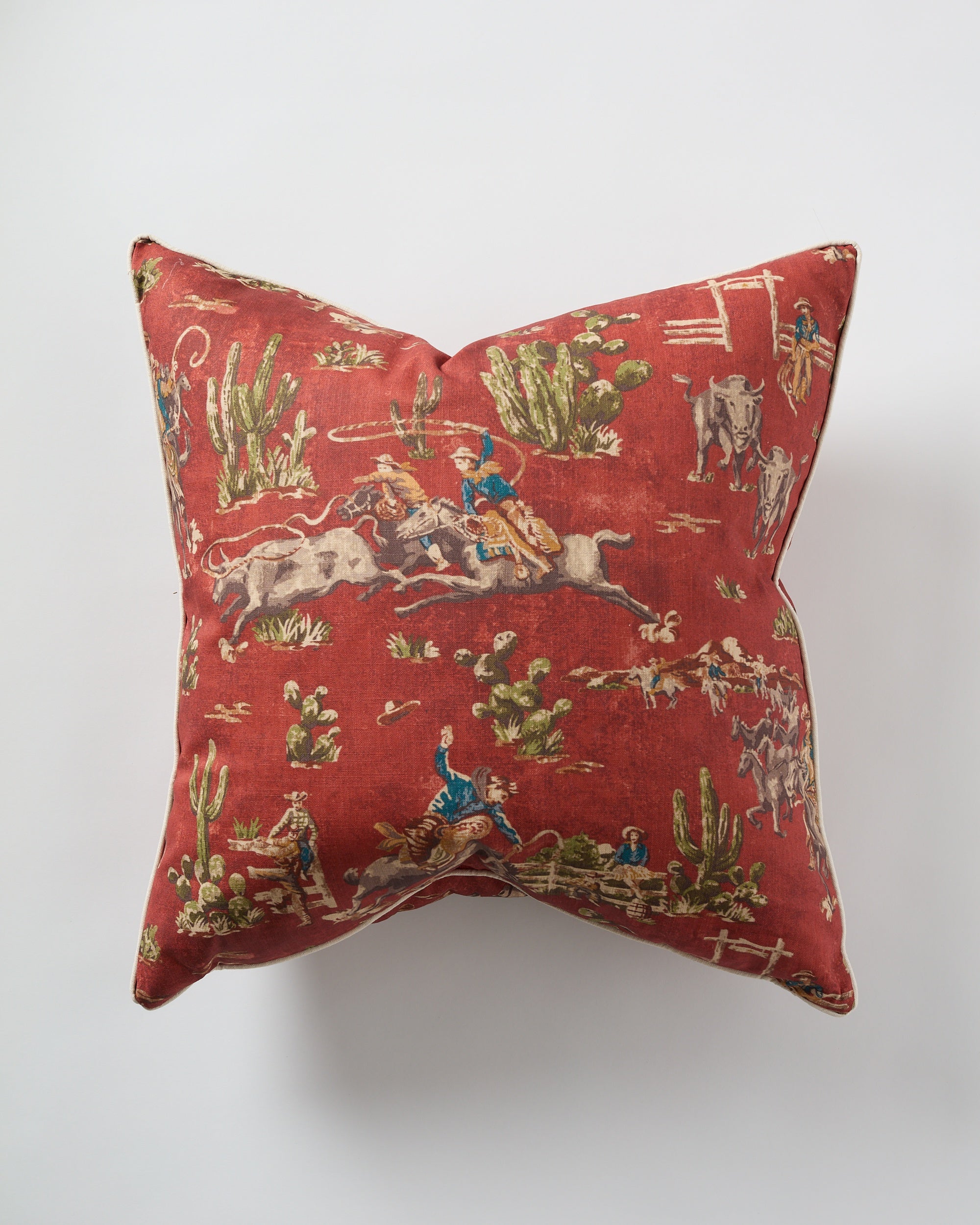 The Design Legacy Red Cowboy Pillow 26x26 features a brick red background with a Western-themed print of cowboys on horseback, lassoing cattle, and scattered cacti.