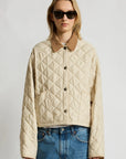 Denimist FAULKNER quilted jacket with snap closure and brown collar, styled with blue jeans and sunglasses.