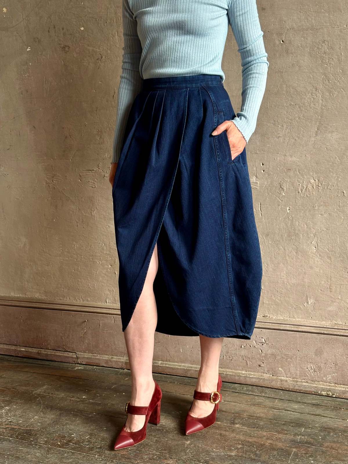 Rachel Comey Sobre Skirt paired with a blue ribbed top and red heels in a modern, textured beige setting.