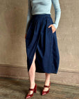 Rachel Comey Sobre Skirt paired with a blue ribbed top and red heels in a modern, textured beige setting.