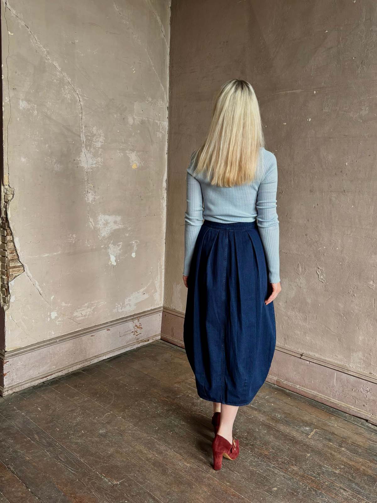 Rachel Comey Sobre Skirt in a rustic room with a woman wearing a blue top against a worn beige wall.