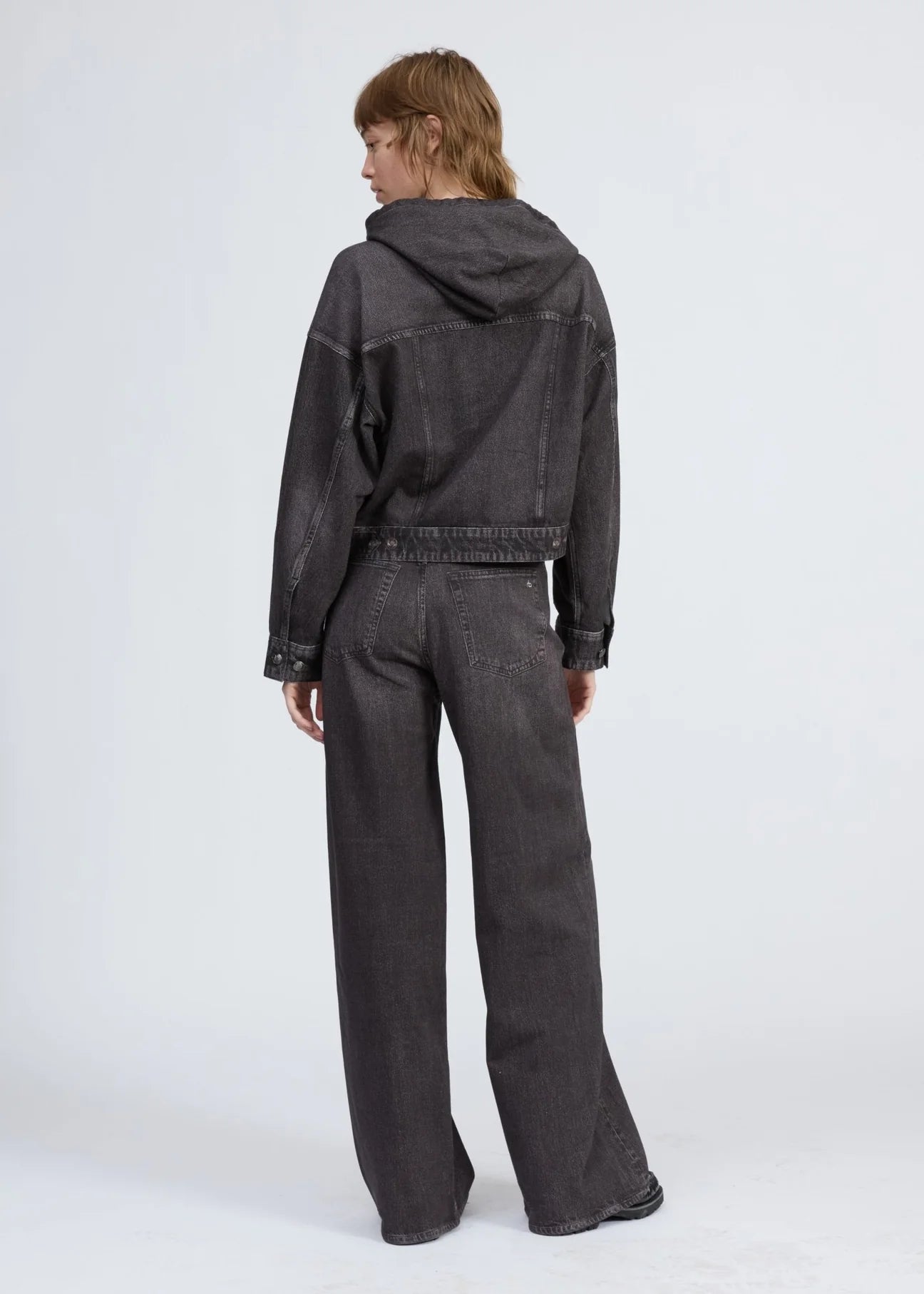 A person with short, light brown hair faces away in a dark gray Rag & Bone miramar terry hood trckr jckt and matching wide-leg jeans, set against a plain light background.