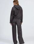 A person with short, light brown hair faces away in a dark gray Rag & Bone miramar terry hood trckr jckt and matching wide-leg jeans, set against a plain light background.