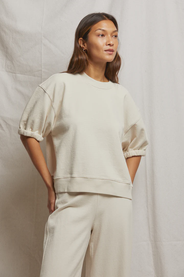 Against a plain background, a person with long, dark hair and a relaxed expression wears the oversized Rebecca 3/4 Puff Sleeve sweatshirt in cream. Made by Perfectwhitetee from cotton fleece, it's paired with matching pants.