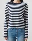 A person wears the Brigitte LS Tee by AMO Denim—navy and white stripes with a chest pocket—paired with relaxed fit blue jeans, against a plain light background. The casual Los Angeles-made look features the face partially out of frame.