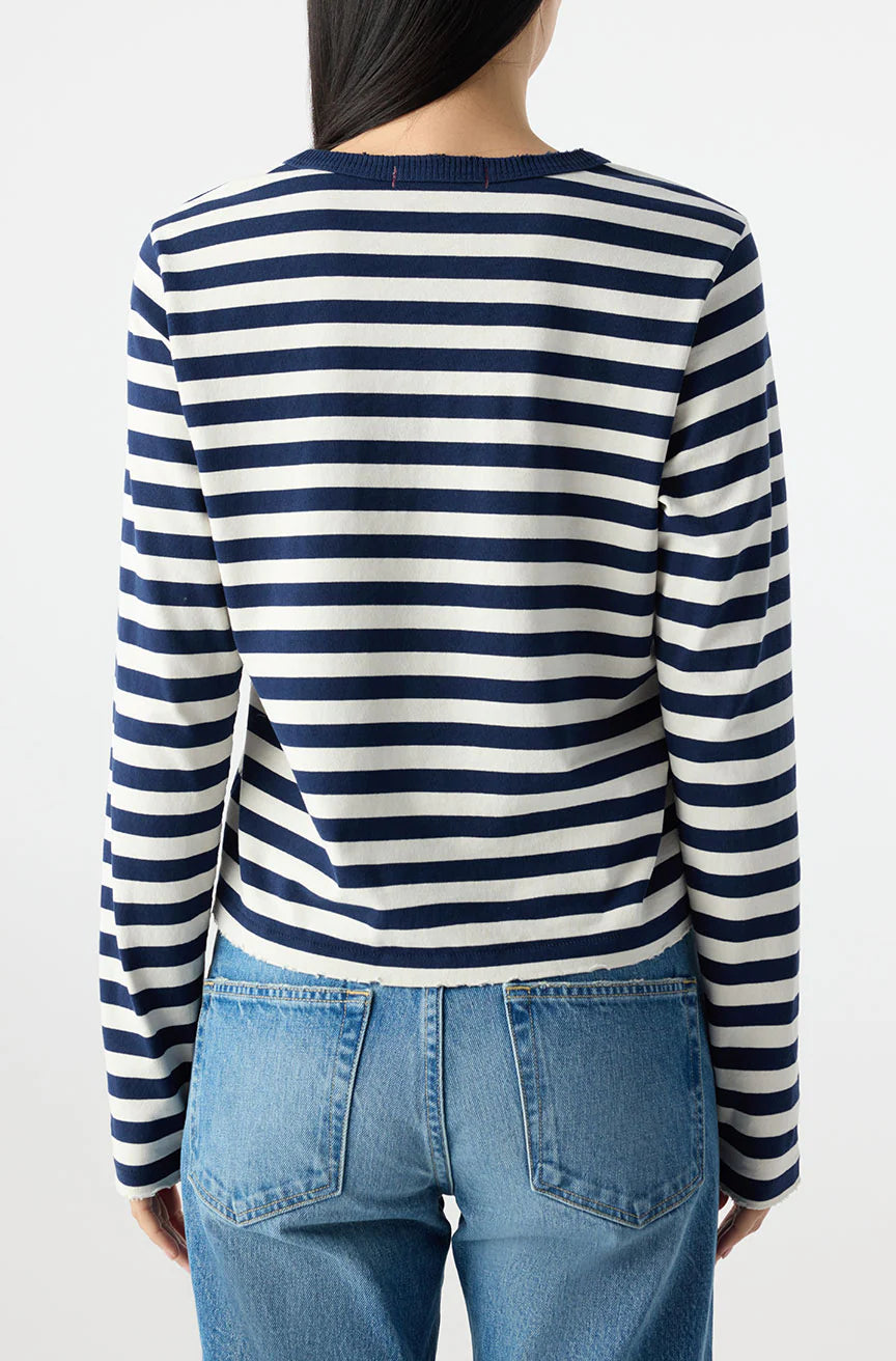 A person with long dark hair, seen from behind, wears the AMO Denim Brigitte LS Tee in navy and white stripes with blue jeans against a plain light background.