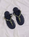 A pair of Flowze FLO Sandals, featuring black leather soles and green and beige knotted rope straps, rest on slightly wrinkled white fabric.
