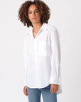 A person with curly hair models the AMO Denim Ruth Oversized Shirt and blue jeans, standing against a plain white background while looking at the camera with a neutral expression.