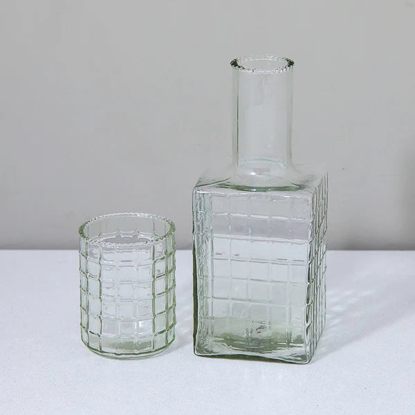 The Be Home Ruffle Glass Bedside Set—a chic clear tumbler and matching square bottle with a grid pattern—rests side by side on a white surface against a plain background.
