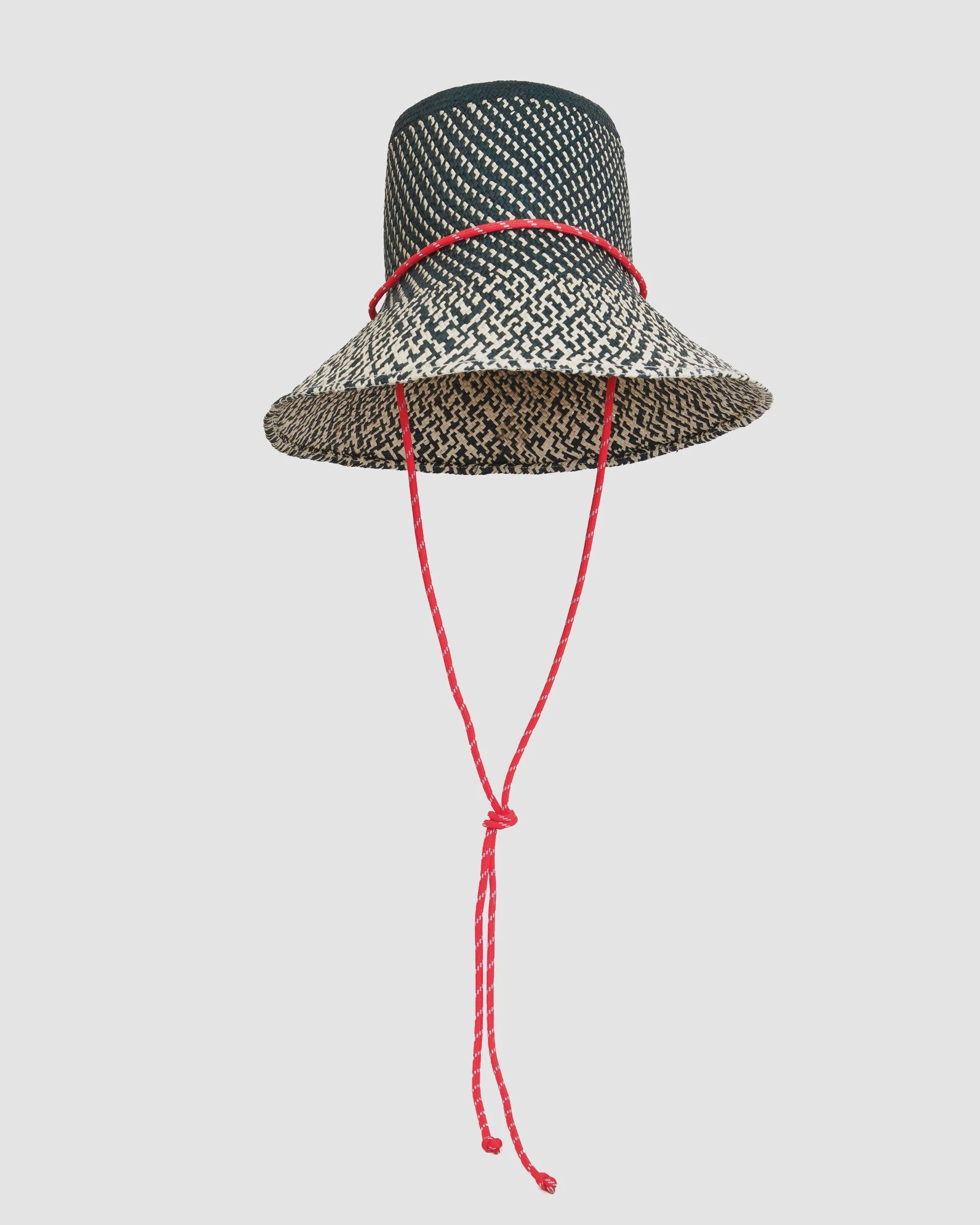 The Clare Vivier Romy Hat is a black and white woven straw rattan hat featuring a wide brim and a red sail cord strap tied in a knot, shown against a plain light background.