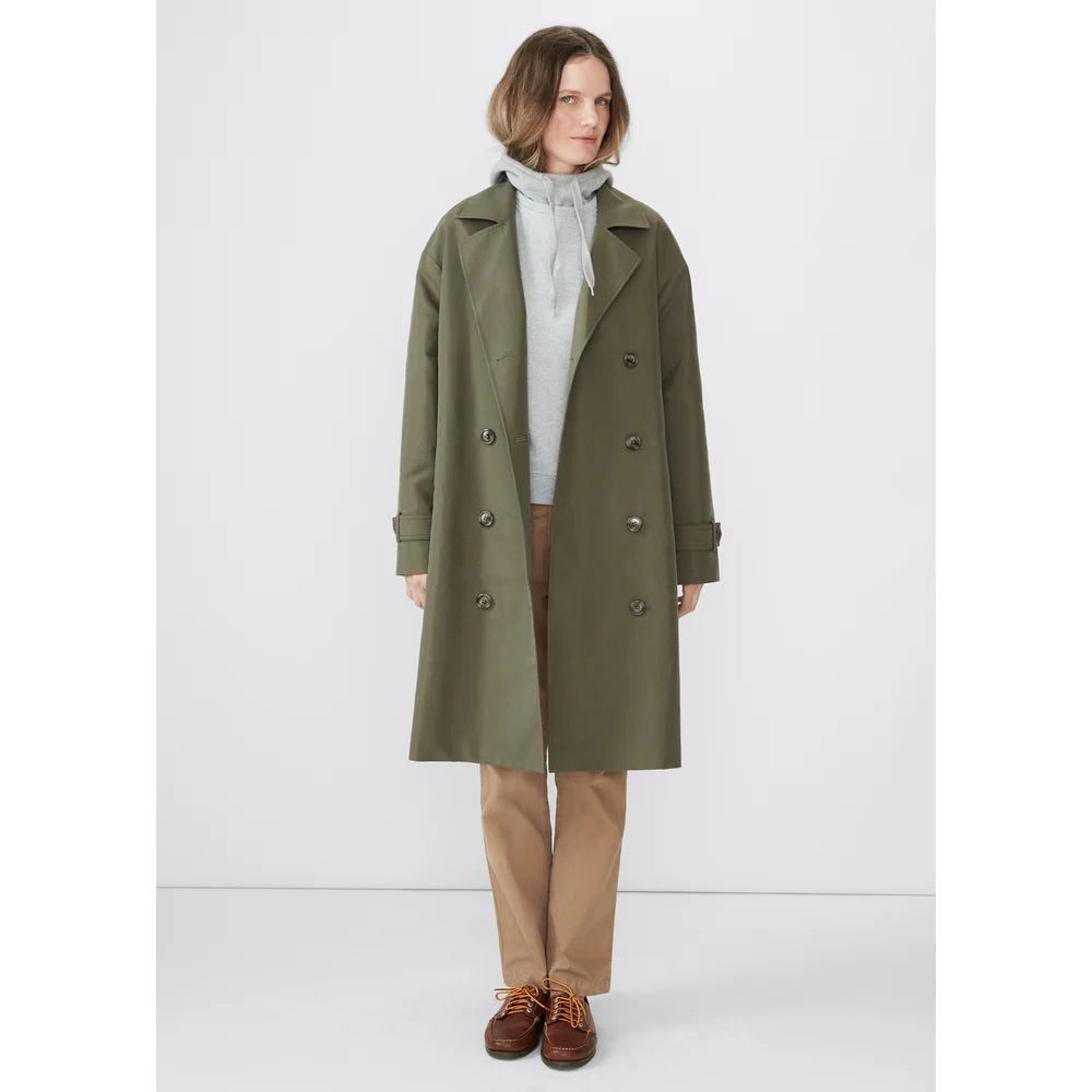 A person wearing The Rox trench by Kule, a chic oversized green trench coat, over a gray hoodie and tan pants stands against a plain background. They are also wearing brown shoes.