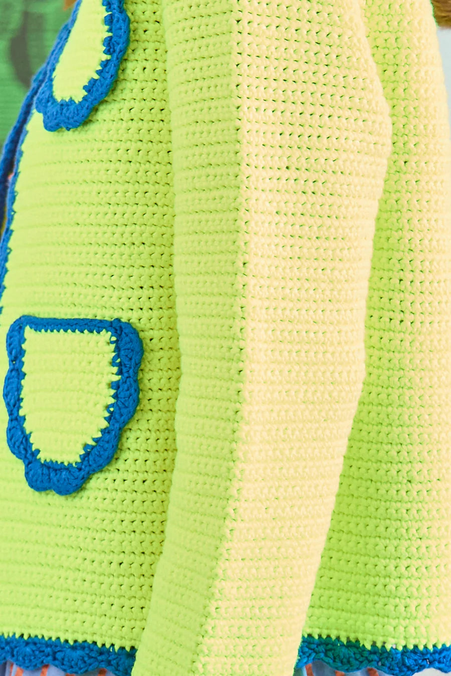 Close-up of a crocheted lime green sweater with blue scalloped trim on the pocket and edges, highlighting detailed stitching similar to the Russell Cardigan by Hunter Bell NYC.